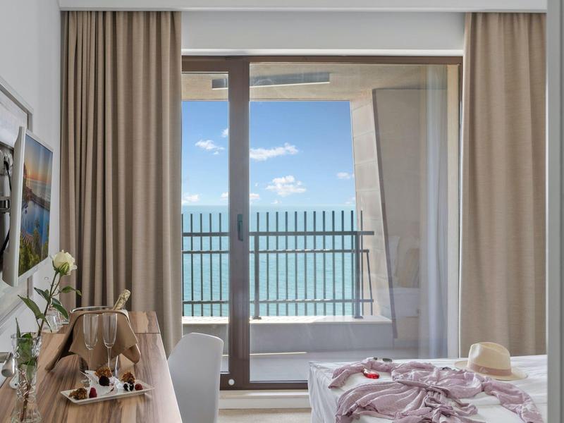 Světle zařízený hotelový pokoj s výhledem na moře skrz velká okna.