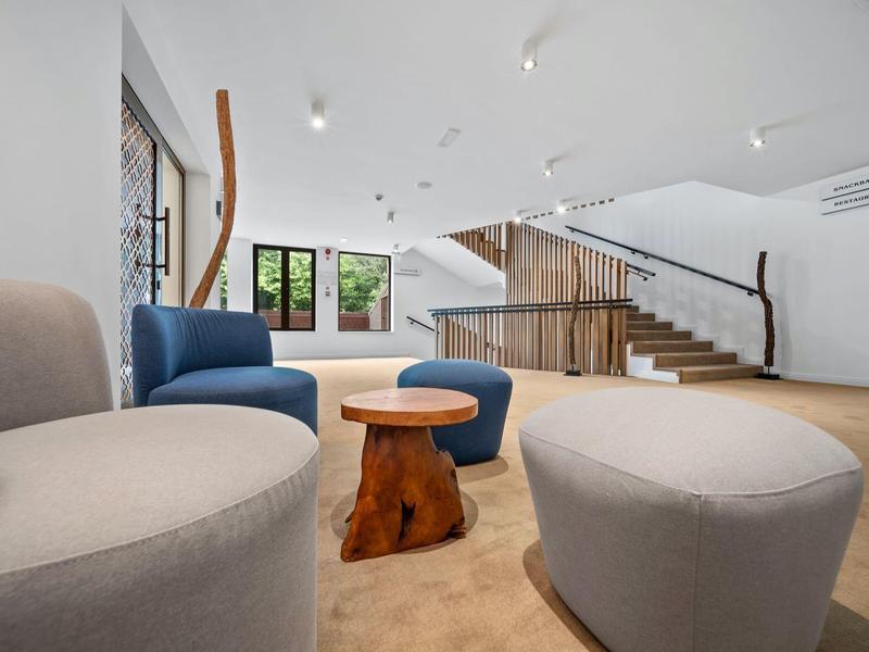 Moderní hotelová lounge s pohodlnými křesly, malým dřevěným stolkem a schodištěm v pozadí.