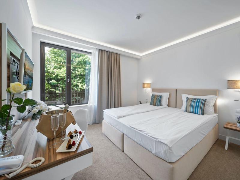 Moderní hotelový pokoj se dvěma jednolůžky, velkými okny a jednoduchou výzdobou.