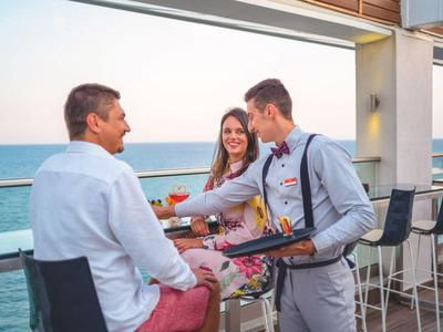 Waiter serves guests on a hotel terrace with sea view at sunset.