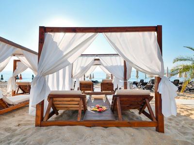 Dos tumbonas de madera bajo una carpa de tela blanca en la playa con vista al mar.