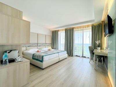 Habitación de hotel luminosa con dos camas individuales, escritorio, televisor de pantalla plana y balcón con cortinas.