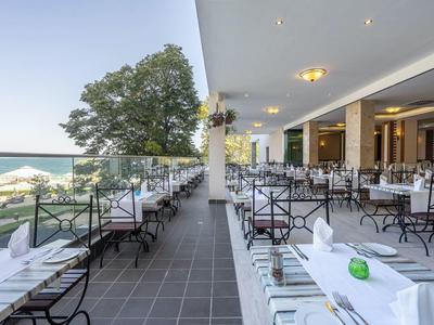 Gran terraza con mesas y sillas preparadas con vista al mar y árboles a la luz del día.