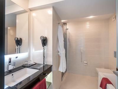 Baño luminoso con ducha, toallas blancas y decoración moderna.