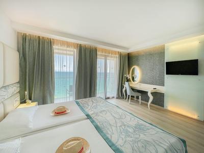 Habitación de hotel luminosa con grandes ventanas con vistas al mar, dos camas individuales y cómoda con espejo.