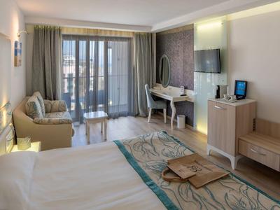 Habitación de hotel luminosa con cama doble, sofá, escritorio y balcón con vista al mar.