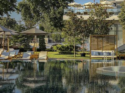 Piscina de hotel con tumbonas, sombrillas y muebles modernos al aire libre rodeada de árboles.