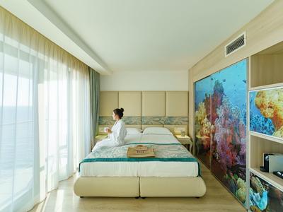 Habitación de hotel moderna con vista al mar, cama grande y mujer cerca de la ventana.