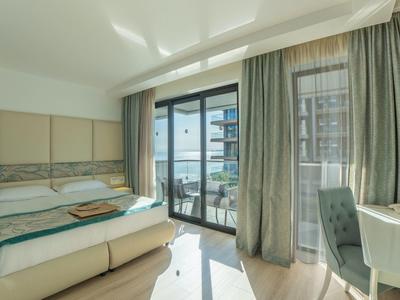 Habitación de hotel luminosa con cama grande y balcón con vista a edificios cercanos.