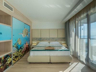 Dormitorio moderno con cama doble, arte mural submarina y ventanas de piso a techo con cortinas.