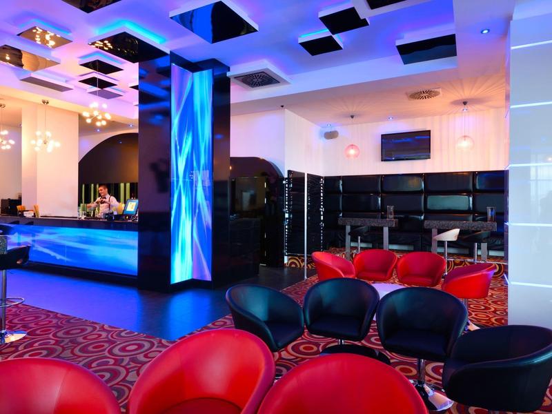 Bar de hotel moderna con mostrador iluminado en azul, asientos rojos y negros y alfombra.