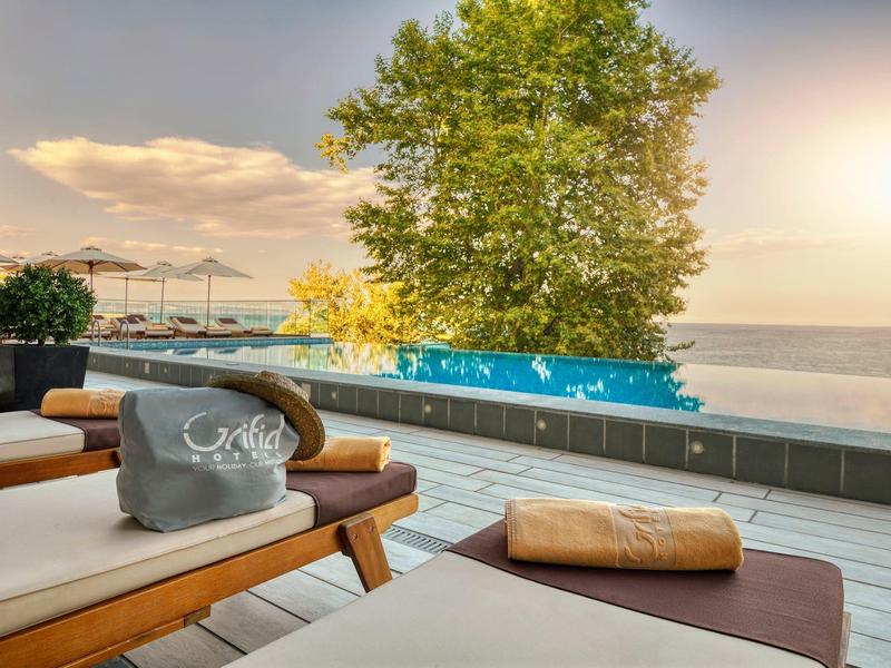 Tumbonas en terraza con vista a la piscina y al mar al atardecer.