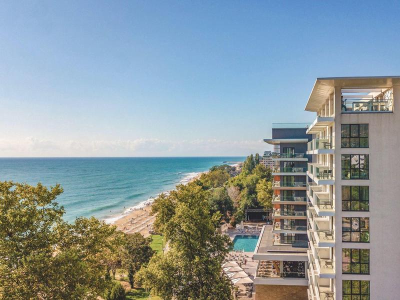 Vista al mar y complejo hotelero moderno con piscina cerca de la costa bajo cielo despejado.