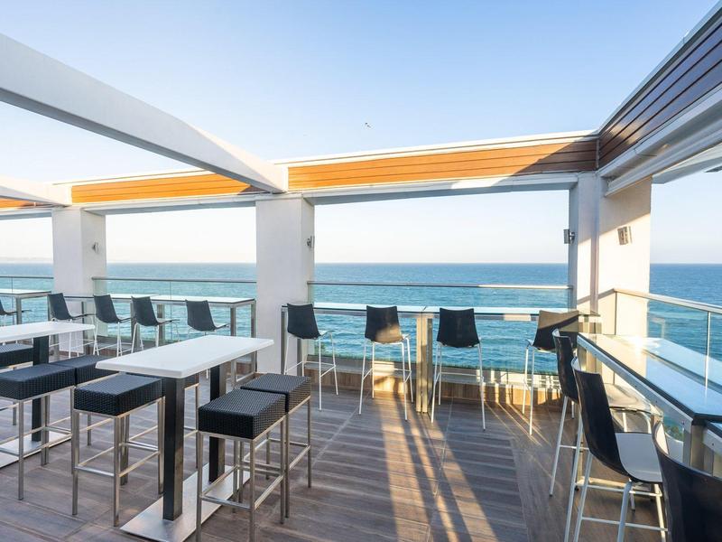 Terraza en la azotea con mesas y sillas con vista al mar en día soleado.