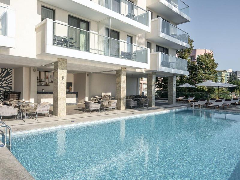 Piscina exterior moderna con tumbonas frente a un edificio de hotel bajo cielo despejado.