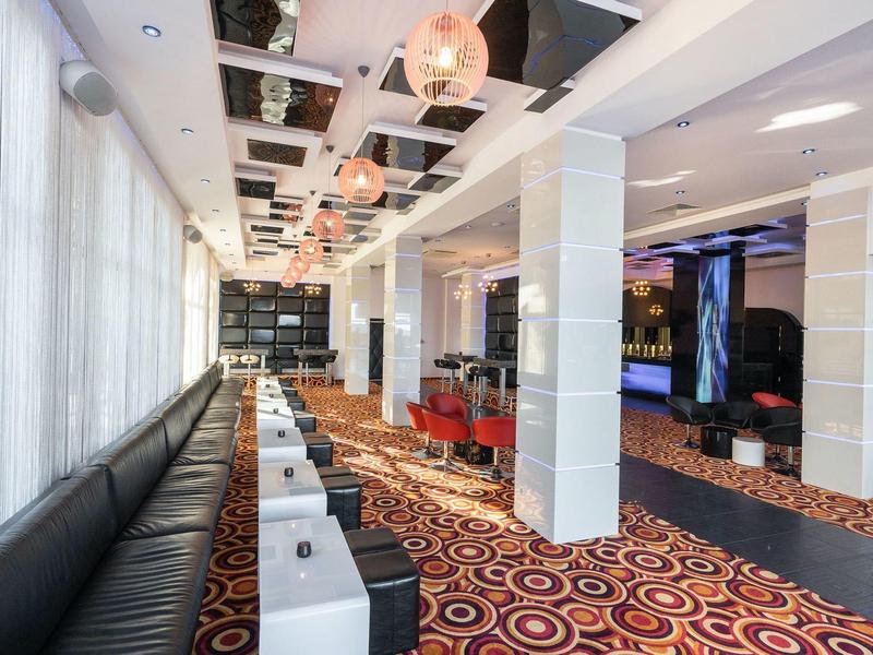 Moderna recepción de hotel con áreas de asientos, alfombra con patrón de círculos y lámparas de techo iluminadas.