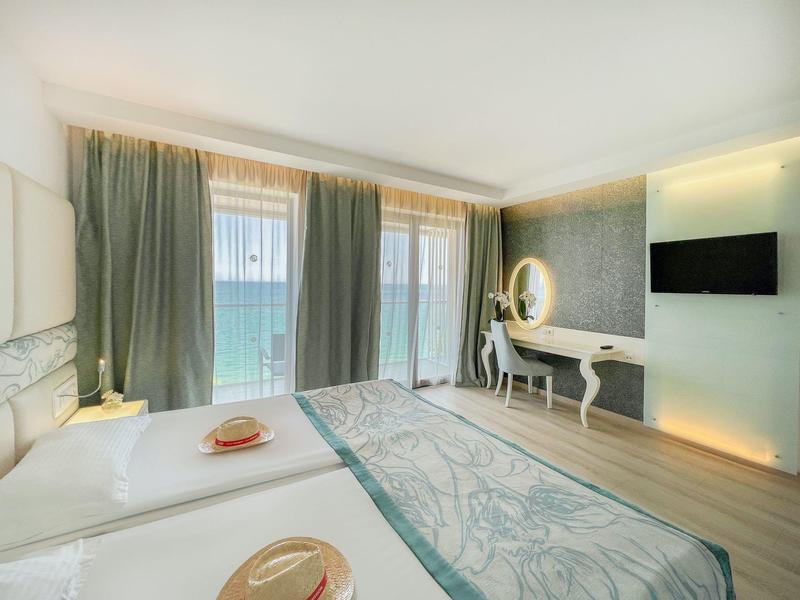 Habitación de hotel luminosa con grandes ventanas con vistas al mar, dos camas individuales y cómoda con espejo.