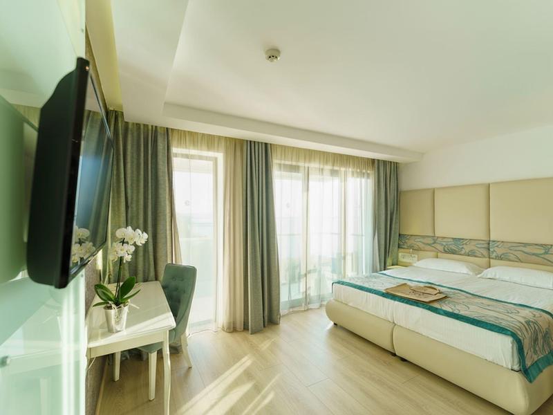 Habitación de hotel luminosa con cama doble, televisor de pantalla plana y grandes ventanas con cortinas.