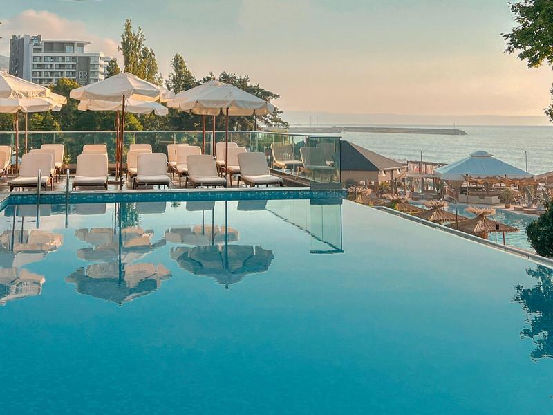 Piscina infinita con tumbonas y sombrillas cerca del mar al atardecer.