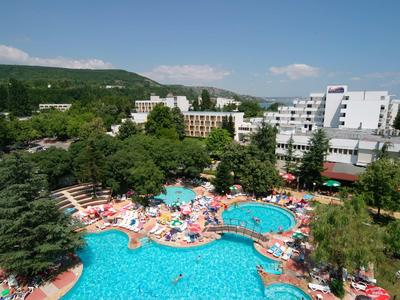 Grande piscine d'hôtel avec parasols et chaises longues, entourée d'arbres verts et de bâtiments de l'hôtel.