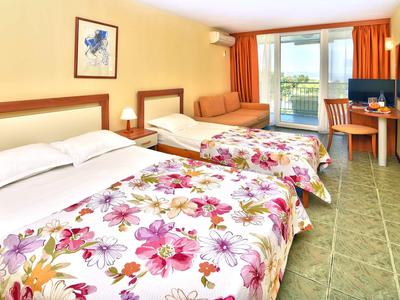 Chambre d'hôtel avec deux lits, literie fleurie, canapé et balcon avec vue sur l'eau