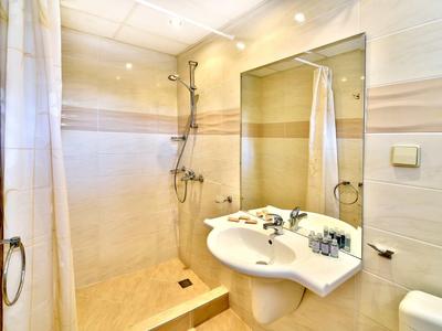 Salle de bain lumineuse avec douche, lavabo, miroir et carrelage beige.