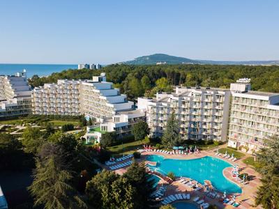 Complexe hôtelier avec plusieurs bâtiments et grande piscine extérieure, entouré d'arbres avec vue sur la mer.