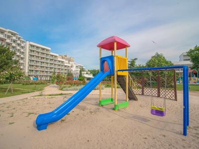 Aire de jeux colorée avec toboggan et balançoire sur du sable devant des immeubles résidentiels et des arbres
