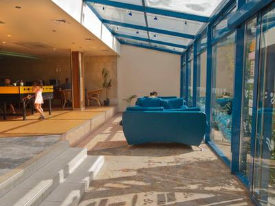 Intérieur avec canapés bleus, toit en verre et accès à un bar d'hôtel