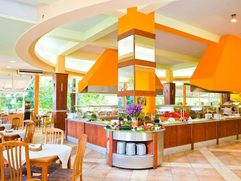 Bright restaurant with wooden chairs and central buffet area under orange hoods.