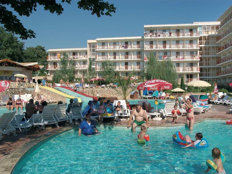 Families enjoy a pool area in front of a multi-story hotel on a sunny day.