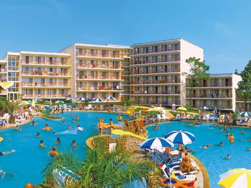 Luxury hotel with large outdoor pool, sun loungers, and umbrellas surrounded by greenery.