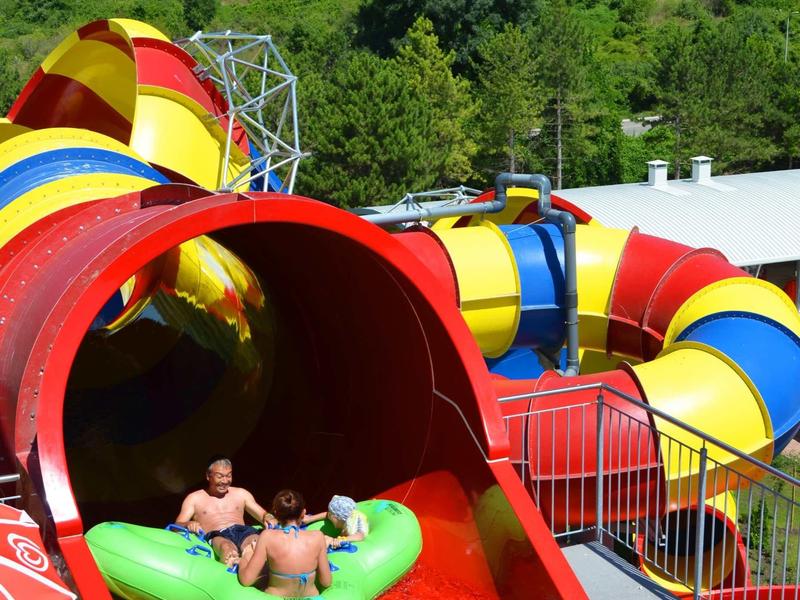 Colorful water slide with two people on a green inflatable raft in a water park.