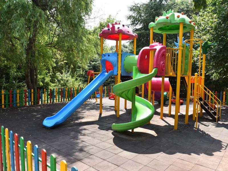 Colorful children's playground with slides and climbing frame surrounded by trees.