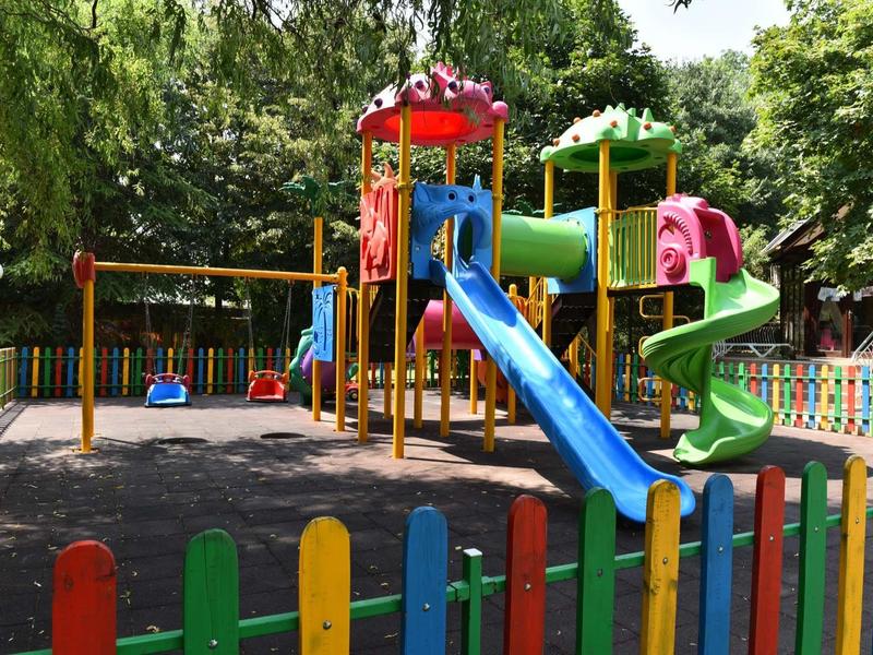 Colorful outdoor playground with slides and swings surrounded by trees.