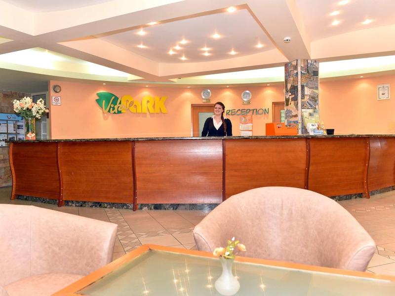 Hotel reception with a person behind the desk and a seating area in the foreground.
