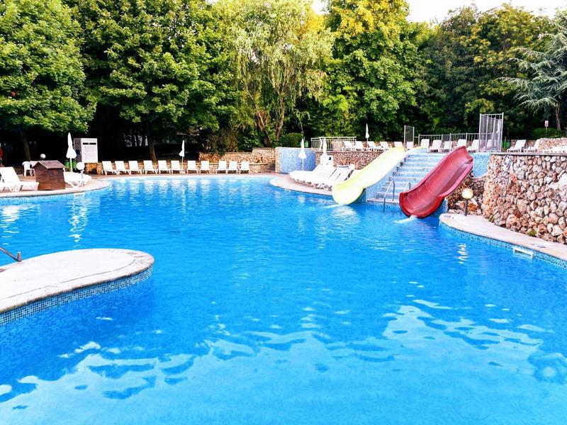 Large outdoor pool with water slides and sun loungers surrounded by trees.