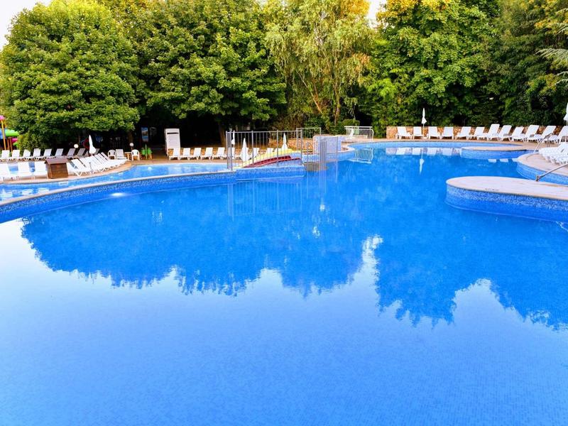 Large blue pool with white lounge chairs and green trees in the background.