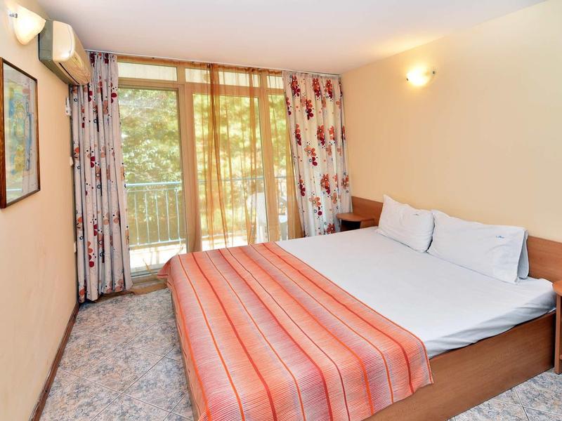 Bright hotel room with double bed, red striped bedspread, and balcony access.