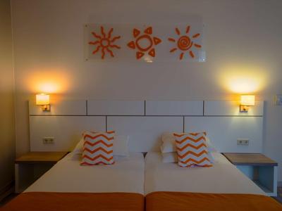 Twin room with two single beds, orange accents, and three sun paintings on the wall.