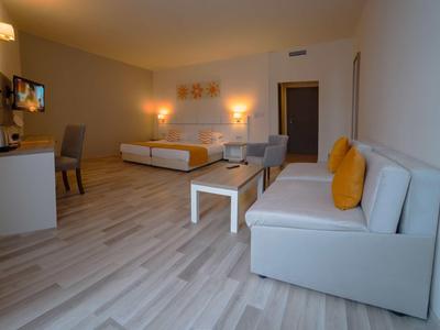 Spacious hotel room with double bed, sofa, desk, and wooden flooring.