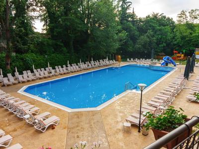 Outdoor swimming pool surrounded by lounge chairs and trees in a green setting.
