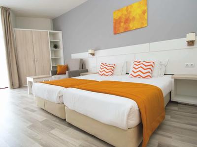 Modern hotel room with two single beds, orange bed runners, and a wardrobe.
