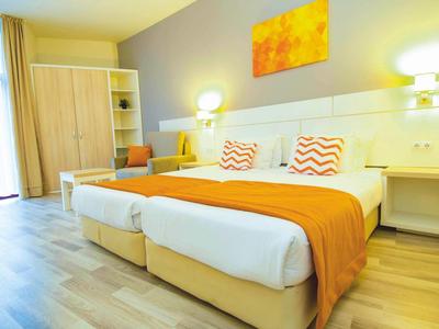 Bright hotel room with two single beds, orange accents, and modern furniture.