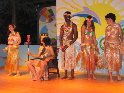 Five people in colorful Hawaiian costumes with grass skirts and flower leis on a stage.