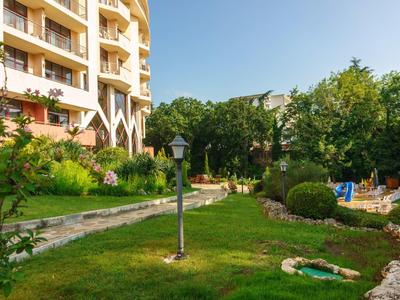 Green hotel garden with pathways, seating areas, and flower decorations under clear sky.