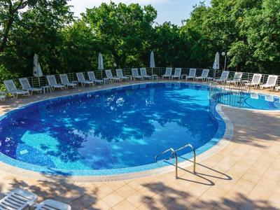 Large round outdoor pool with sun umbrellas and lounge chairs, surrounded by trees.