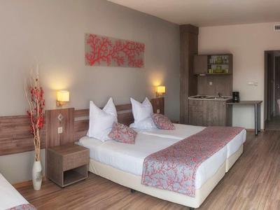 Hotel room with double bed, single bed, desk, kitchenette, and wooden floor