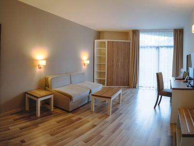Bright hotel room with sofa, wooden tables, wardrobe, and desk by the window