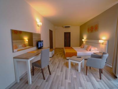 Bright hotel room with double bed, desk, chairs, and large mirror.